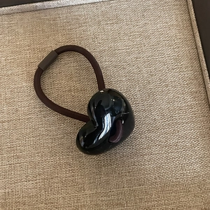 Close-up of a brown elastic hair tie featuring a glossy black heart-shaped pendant charm