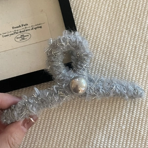 Détail d'une pince à cheveux en peluche grise avec fils argentés et grosse sphère métallique
