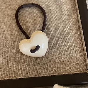 Close-up of a cream resin heart charm on a brown elastic hair tie in a display box
