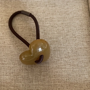 Detail of a jelly amber heart charm on a brown elastic hair tie with woven texture background