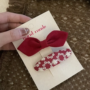 Detail view of festive red bow hairclip and floral embroidery clip on display card