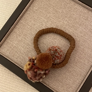 Forest style hair tie with colorful yarn balls and brown plush beads on linen background