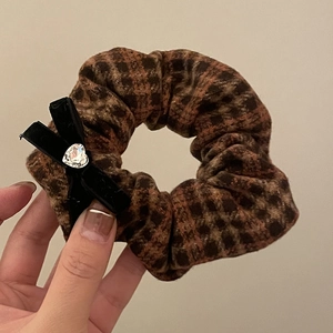 Detailed view of brown plaid scrunchie with a black velvet bow and heart-shaped rhinestone