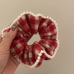 Vue détaillée du chouchou à carreaux rouges avec de mignons pompons blancs en bordure