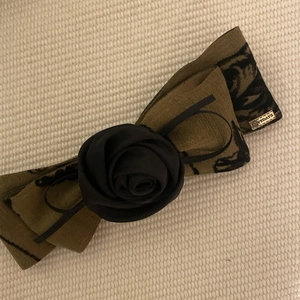 Olive green floral bow hair clip with black rose detail and golden brand tag
