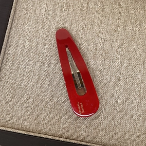 Barrette en acétate bordeaux poli avec lettrage doré sur texture beige tressée
