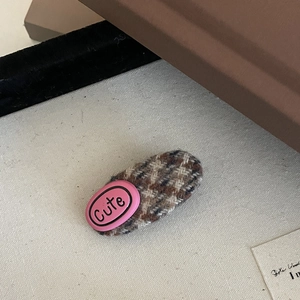 Close-up of a brown tweed plaid hair clip with a pink label featuring Cute text decoration