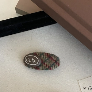 Close-up of a tweed plaid BB hair clip with a cute brown oval letter decoration