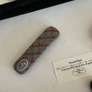 Detailed macro view of a plaid wool hair clip featuring a cute badge and textured fabric