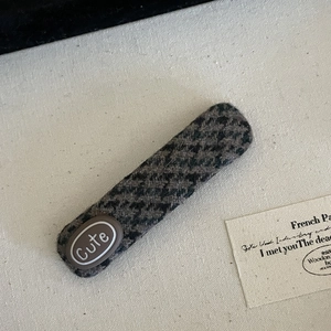 Close-up of a grey houndstooth wool hair clip with a brown Cute text decorative patch