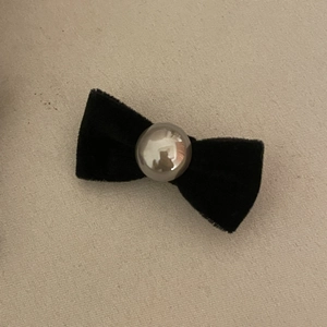 French style black velvet bow hair clip with central pearl bead on textured background