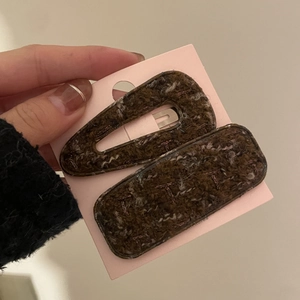 Set of two coffee brown wool hair clips with purple embroidery on a display card