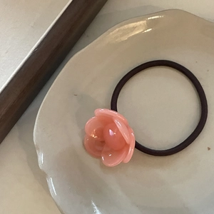 Detail of pink resin camellia flower hair tie with high-elastic band on beige ceramic plate