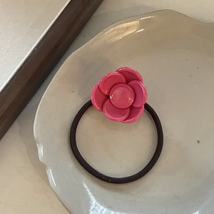Detail of pink resin camellia flower hair tie on a white ceramic plate