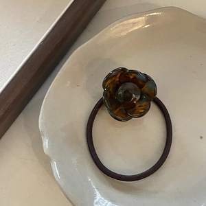 Detailed view of amber acetate camellia flower hair tie on a white ceramic tray