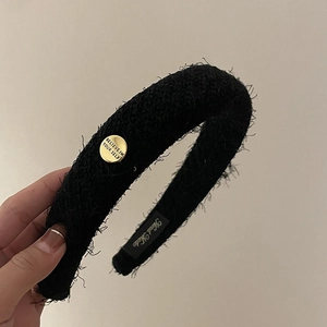 Détail d'un serre-tête en peluche noire avec boucle dorée et texte de motivation gravé