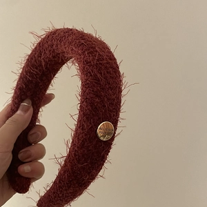 Détail d'un serre-tête en peluche bordeaux avec une plaque dorée gravée de messages