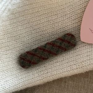 Macro shot of white plush knitted hair clip with grey and red diagonal stripe patch