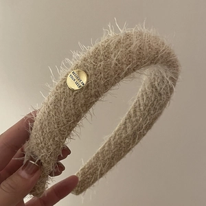 Détail du serre-tête en peluche beige avec un bouton doré gravé Believe In Yourself