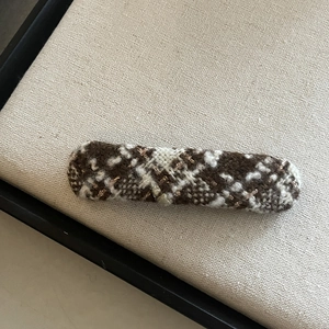 Close-up of brown and white checkered wool hair clip on beige linen display tray