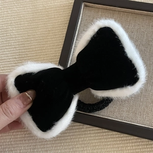 Detailed close-up of a black velvet bow hair clip with white faux fur trim and elastic band