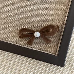 Brown velvet bow hair clip with central pearl detail on a textured display board
