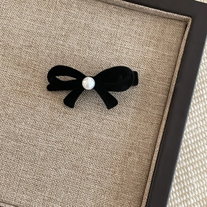 Close-up of black velvet bow hair clip with a faux pearl center on linen surface