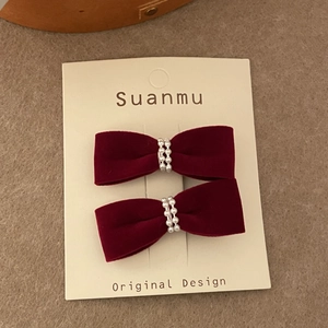 Close-up of velvet wine red bow hair clips with pearls on a textured background