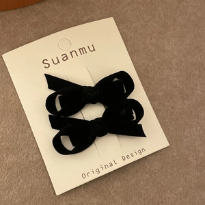 Close-up of a pair of black velvet bow hair clips on a white display card original design