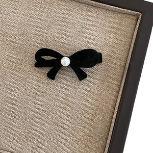 Elegant black velvet bow hair clip with a centered pearl bead on a textured background