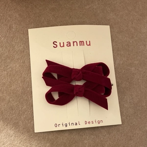 Detail shot of two burgundy velvet bow hair clips on premium cream display card