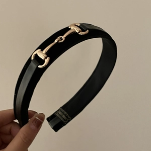 Detail of a black leather headband with a distinctive gold metal horsebit buckle design