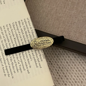 Vintage-Haarspange aus schwarzem Samt mit ovaler Goldplakette auf einem offenen Buch