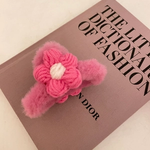 Handmade pink plush hair claw clip with woven floral detail on a fashion book