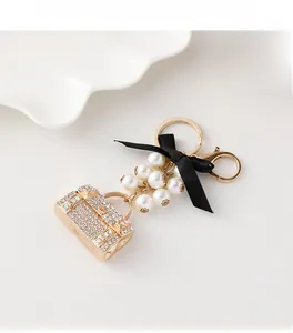 Détail d'un porte-clés sac à main doré avec strass, perles blanches et nœud en satin noir