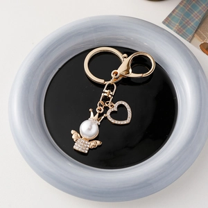 Elegant gold angel keychain with heart pendant and white pearl bead on ceramic plate