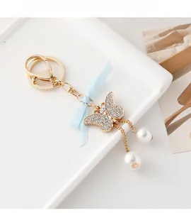Détail du porte-clés papillon doré avec perles blanches et nœud en ruban bleu