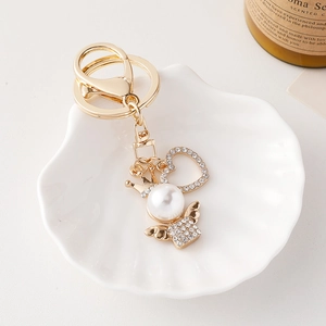Elegant gold angel keychain with heart crown charm and pearls on a white shell tray