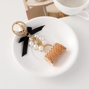 Porte-clés sac à main doré matelassé avec perles blanches et nœud noir sur une assiette