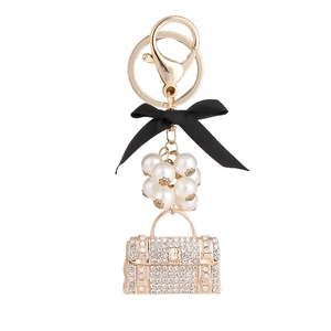 Porte-clés sac à main doré avec nœud noir, perles blanches et strass brillants