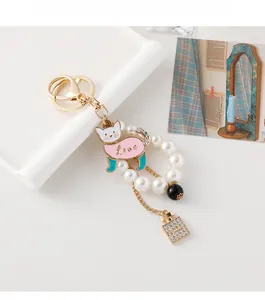 Detail of a cat pearl keychain with a gold lobster clasp and a sparkly perfume bottle charm