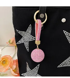 Close-up of sparkling pink rhinestone ball bag charm with gold metal clasp on a black tote
