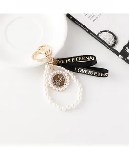 Détail d'un porte-clés perles élégant avec anneau doré et ruban noir sur un bureau blanc