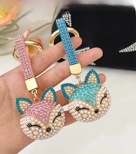 Handheld view of rhinestone and pearl fox keychains in pink and blue with gold rings