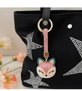 Detailed close-up of a pink pearl fox keychain with rhinestones on a black canvas bag