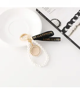 Détail d'un élégant porte-clés doré avec perles blanches et ruban noir à texte doré
