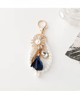 Close-up of elegant flower keychain with white pearls, blue petals and gold crystal drop