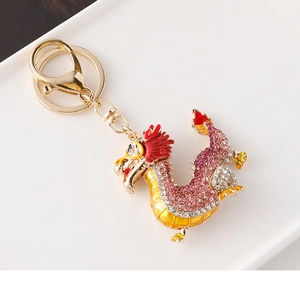 Détail d'un porte-clés dragon doré avec strass roses et émail sur un plateau blanc