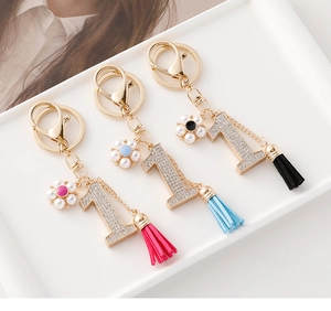 Détail de trois porte-clés numéro un avec strass, fleurs de perles et pompons colorés