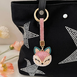 Exquisite fox keychain with pink crystals and pearls on a black bag with floral decor